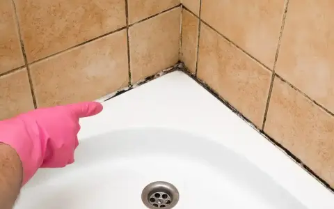 Main rose avec un gant, montrant la moisissure sur le joint de la baignoire. Il est temps d'enlever moisissure joint.