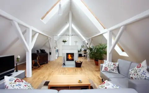 Aménagement comble 30m2 : salon cosy avec cheminée, canapé gris, parquet clair et poutres apparentes.