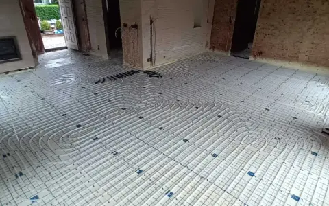 Installation d'un plancher chauffant en cours de renovation. Les tuyaux blancs sont posés sur des panneaux isolants, prêts à être recouverts.