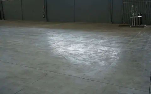 Vaste entrepôt avec une dalle béton qui part en poussière, marquée par des traces de passage.