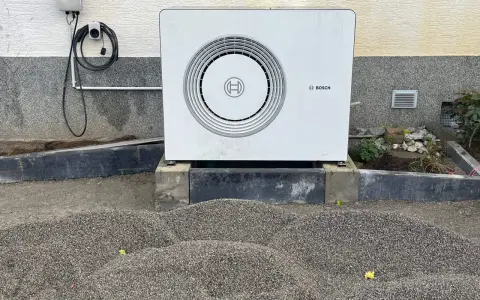 Unité extérieure d'une chaudière à condensation Bosch, installée sur des blocs de béton, avec un chargeur mural à proximité.