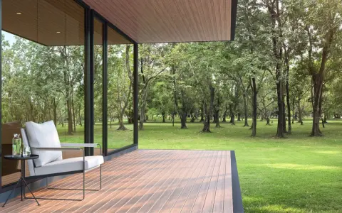 Une terrasse moderne avec un revêtement de terrasse en résine, offrant une vue paisible sur une forêt verdoyante. Un fauteuil confortable invite à la détente.