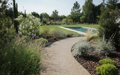 Une allée de jardin originale serpente vers une piscine, bordée de lavande, de fleurs blanches et d'arbustes verts.