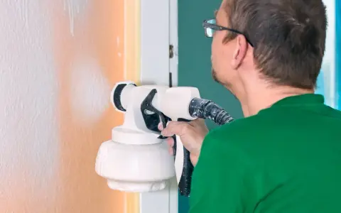 Un homme en t-shirt vert utilise un pistolet pour peindre un mur en orange.