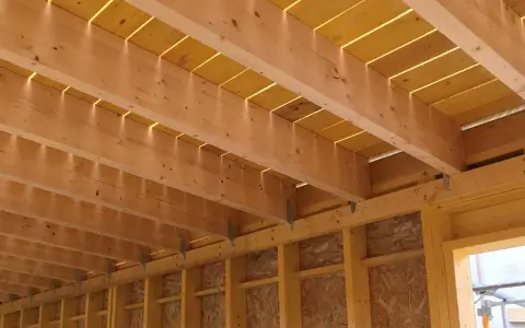 Vue détaillée de comment réaliser le solivage d'un plancher d'étage : poutres en bois, panneaux jaunes et supports métalliques.