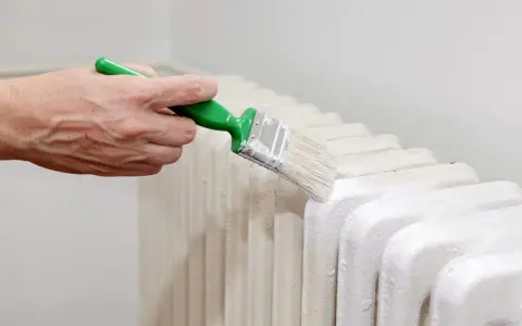 Main d'une personne peignant un radiateur en fonte avec une brosse.