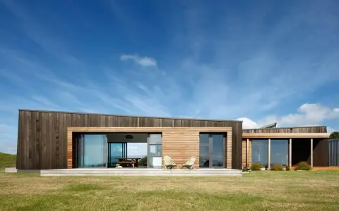 Maison moderne en bois avec grande baie vitrée, deux chaises invitantes sur la terrasse. Une extension maison container stylée.