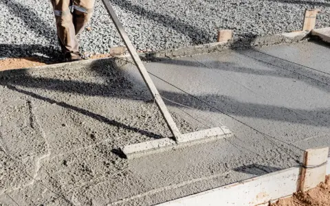 Un ouvrier utilise un râteau pour lisser du béton frais, étape essentielle pour faire une dalle béton solide.