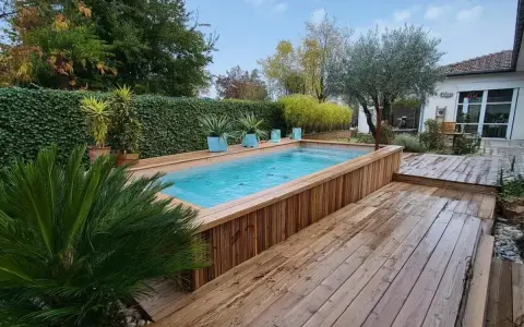 Aménagement abord piscine hors sol en bois, avec terrasse et végétation luxuriante.