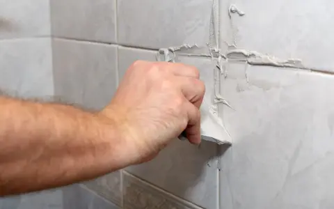 Main tenant enlève du joint de carrelage sec avec une spatule.
