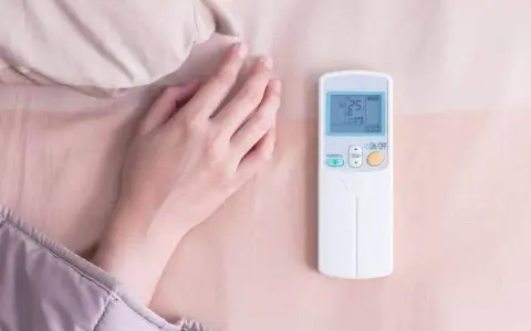 Main tenant ajuste la température clim pour dormir. La télécommande affiche 25 degrés.