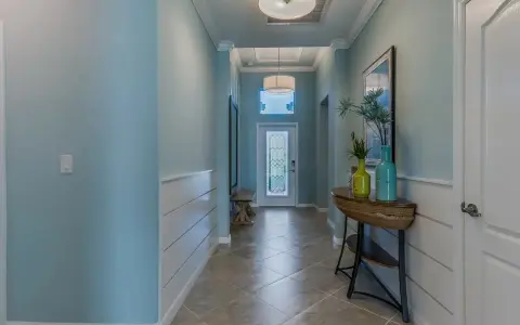 Un couloir lumineux avec une peinture de couloir 2 couleurs : bleu ciel et blanc. Un banc, une console avec des vases et une porte vitrée ornent cet espace accueillant.
