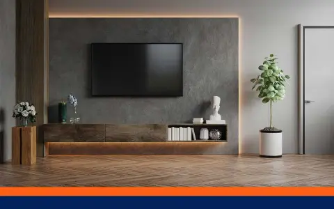 Un salon moderne avec une TV fixée au mur sans voir les fils. Un meuble bas en bois, des livres et une plante verte complètent la décoration.
