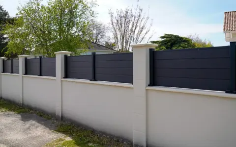 Un mur privatif moderne en composite gris, surmonté de poteaux en pierre, assure l'intimité. Distance à respecter pour une belle clôture.