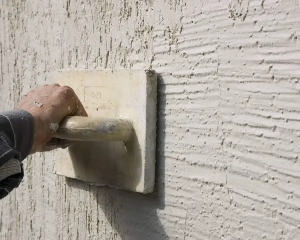 Main d'un artisan appliquant un enduit projeté texturé. Le prix au m2 de ce type de finition est souvent demandé.