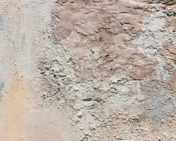 Texture d'un mur extérieur dégradé, montrant des zones de salpêtre et d'enduit écaillé, une cause visible de détérioration.