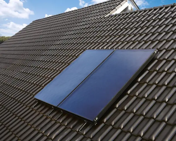 Deux panneaux de chauffage solaire thermique installés sur un toit en tuiles sombres, sous un ciel bleu.