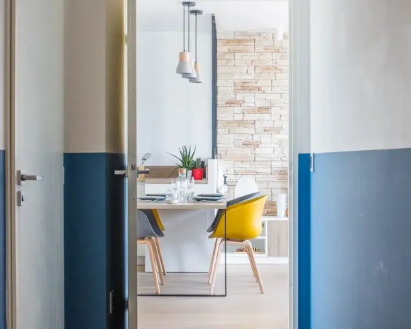 Peinture bicolore sur les murs d'un couloir et de portes, ouvrant sur une salle à manger moderne avec des chaises colorées.
