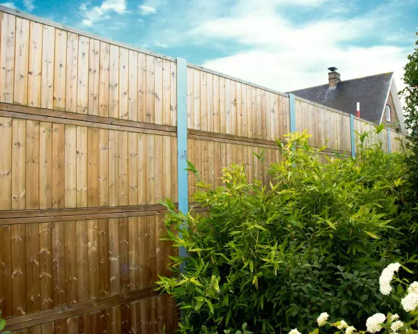 Clôture anti bruit en bois, haute et solide, protégeant un jardin verdoyant. Le ciel bleu et les nuages ajoutent une touche de sérénité.