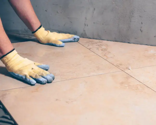 Pose de carrelage avec des gants, assurant l'étanchéité sur carrelage existant.