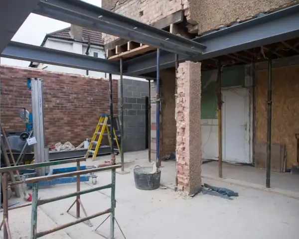 Travaux de rénovation : agrandir ouverture mur porteur avec poutres métalliques. Échafaudages, briques et outils sur le chantier.