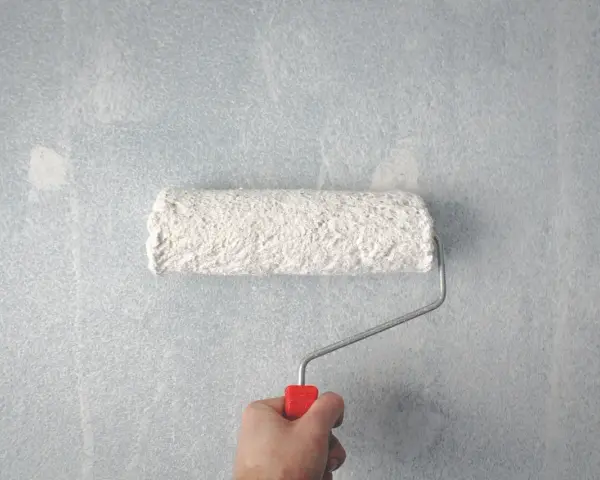 Main tenant rattraper trace de rouleau peinture sur mur bleu clair.