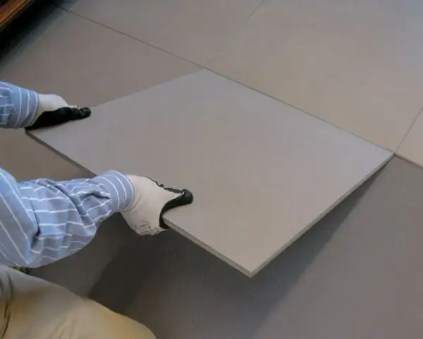 Pose d'une nouvelle dalle pour coller du carrelage sur du carrelage. Les mains gantées ajustent la pièce sur le sol existant.
