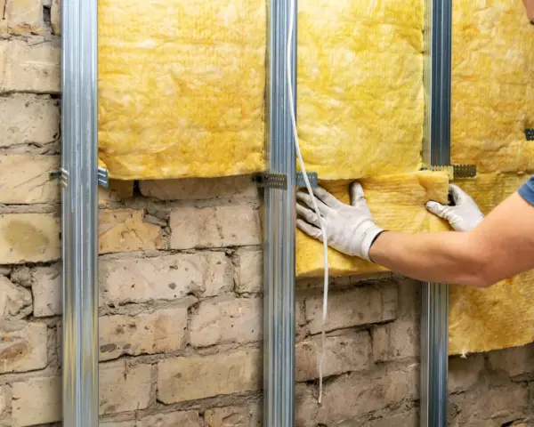 Un ouvrier installe une laine de verre jaune sur une structure métallique fixée à un mur de briques, améliorant l'isolation phonique.