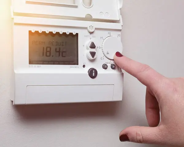Main d'une femme ajustant un cee thermostat connecté affichant 18.4°C.