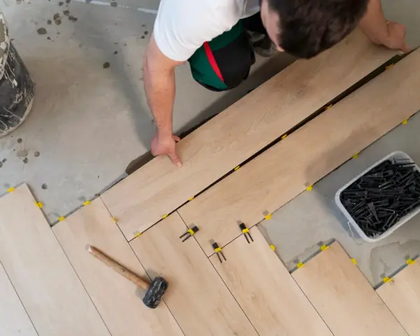 Pose d'un carrelage imitation bois sur un plancher. Un ouvrier pose les lames, des cales jaunes et noires assurent l'espacement.