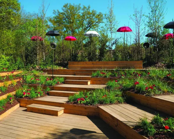 Un jardin aménagé avec des terrasses en bois et une **profondeur marche escalier extérieur** sur plusieurs niveaux, décoré de tulipes rouges et de parasols colorés.
