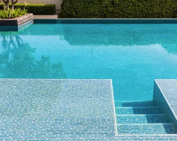 Élégante rénovation piscine mosaïque bleue, avec des marches carrelées et une végétation luxuriante.