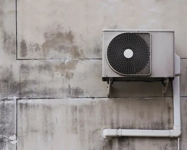 Unité extérieure d'une pompe à chaleur air air fixée sur un mur en béton fissuré et taché.