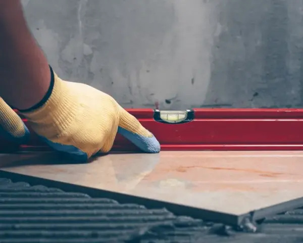 Pose d'un carrelage avec un niveau à bulle pour vérifier l'épaisseur du carrelage et de la colle.