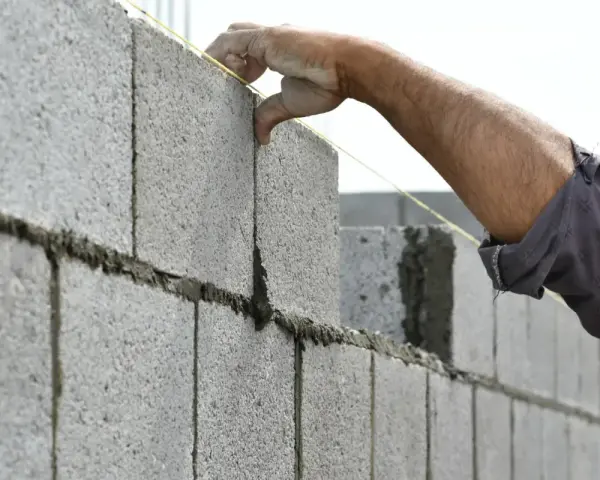 Pose d'un parpaing pour un mur de 25m. Le maçon ajuste la brique avec précision.