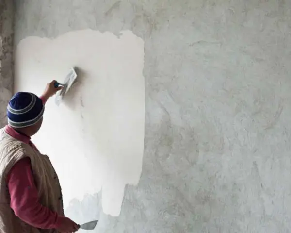 Un artisan applique un enduit chaux sable intérieur sur un mur avec une truelle. La texture naturelle du mortier est visible.