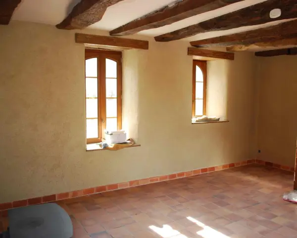 Intérieur d'une pièce aux poutres apparentes, murs en chaux chanvre pour une isolation naturelle, sol carrelé.