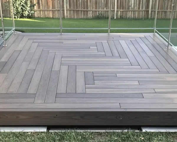 Une belle pose terrasse bois sur terre, avec un motif en chevrons moderne et des garde-corps en verre.