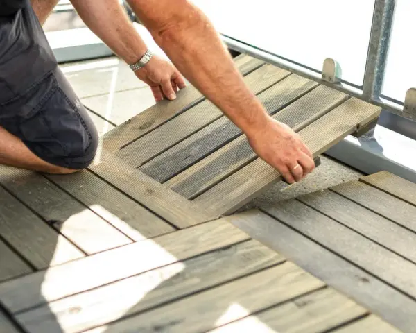 Un homme installe des dalles de terrasse en bois sur son balcon. Une belle idée sol balcon pour un espace extérieur accueillant.