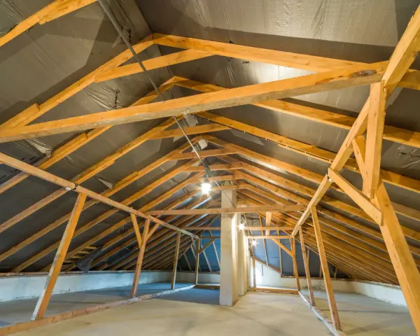 Charpente de grenier en bois, avec une bâche noire recouvrant le toit, suggérant une isolation rampant par l'intérieur en cours.