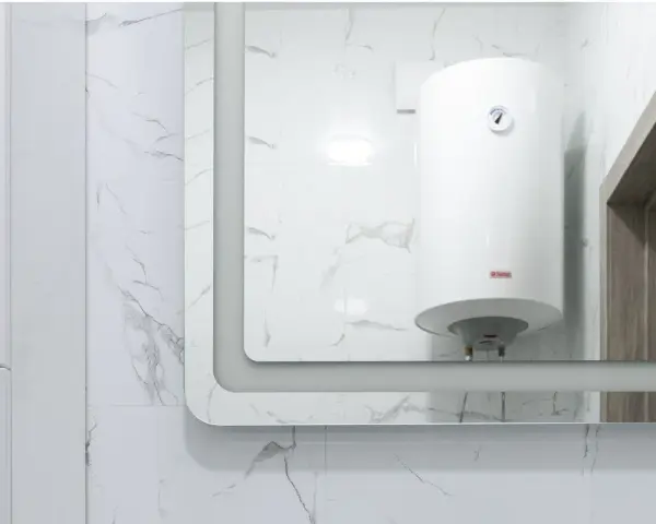 Gros chauffe-eau blanc, une chaudière micro accumulation, reflété dans un grand miroir, sur fond de carrelage marbré.