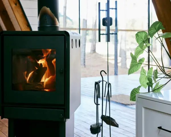 Un poêle à bois MCZ crépitant dans un chalet moderne, avec une grande baie vitrée donnant sur la forêt. Un avis positif s'impose pour ce coin cosy.