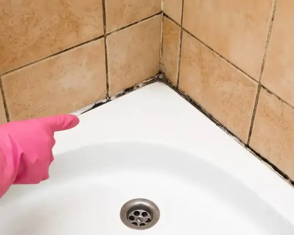 Main rose avec un gant, montrant la moisissure sur le joint de la baignoire. Il est temps d'enlever moisissure joint.