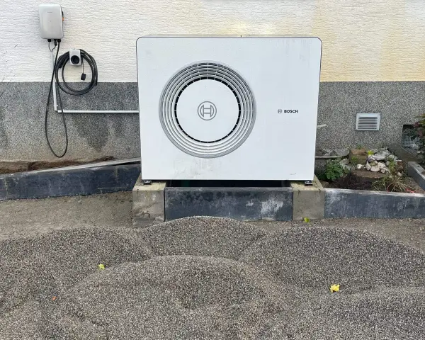 Unité extérieure d'une chaudière à condensation Bosch, installée sur des blocs de béton, avec un chargeur mural à proximité.
