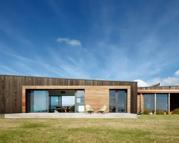 Maison moderne en bois avec grande baie vitrée, deux chaises invitantes sur la terrasse. Une extension maison container stylée.