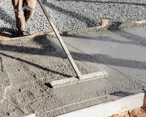 Un ouvrier utilise un râteau pour lisser du béton frais, étape essentielle pour faire une dalle béton solide.