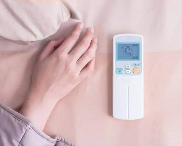 Main tenant ajuste la température clim pour dormir. La télécommande affiche 25 degrés.