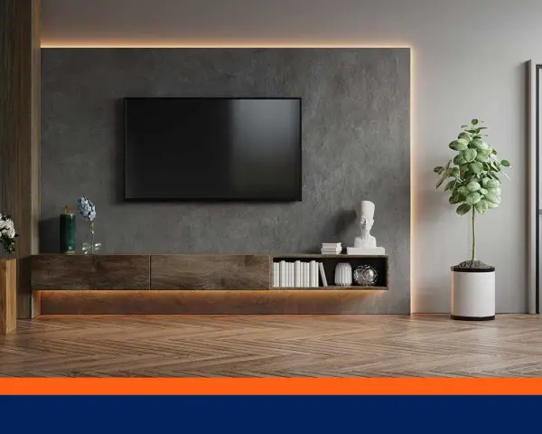 Un salon moderne avec une TV fixée au mur sans voir les fils. Un meuble bas en bois, des livres et une plante verte complètent la décoration.