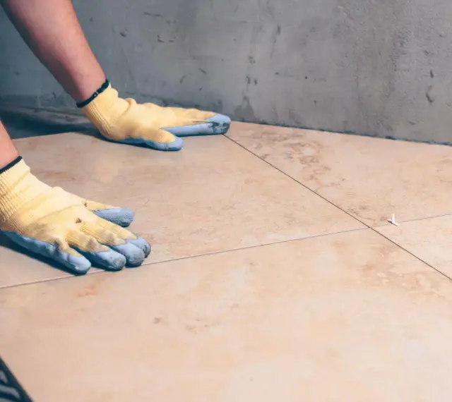 Pose de carrelage avec des gants, assurant l'étanchéité sur carrelage existant.