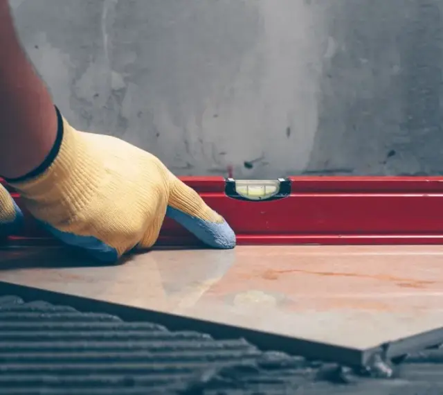 Pose d'un carrelage avec un niveau à bulle pour vérifier l'épaisseur du carrelage et de la colle.
